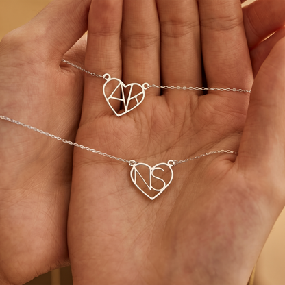 Two silver heart initial necklaces held in hand
